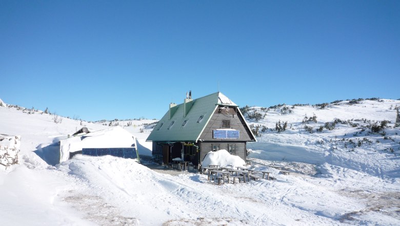 Neue Seehütte, © Neue Seehuette, Foto Doris Eggl Eine Berghütte im Schnee mit Solarpanelen und blauem Himmel.