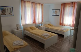 TDR-Gasthof schwarzer Adler- Schlafzimmer, © Márton Varga Drei Einzelbetten in einem hellen Zimmer mit gelber Bettwäsche und bunten Vorhängen.