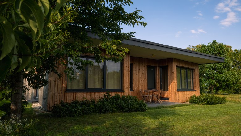 Grafenegg Cottages, © Niederösterreich Werbung / Maximilian Pawlikowsky Ein modernes Holzhaus mit großen Fenstern, umgeben von Bäumen und Rasen.