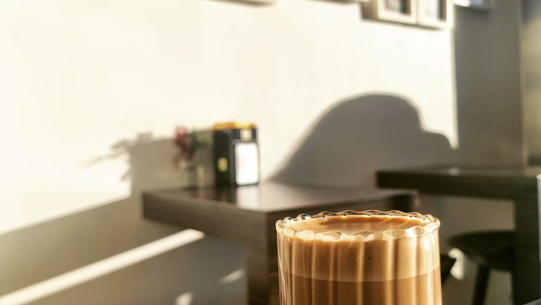 TDR-EgontoGo innen, © Yana Tereshchenko Ein Glas Kaffee auf einem Tisch in einem Café mit Bilderrahmen an der Wand im Hintergrund.