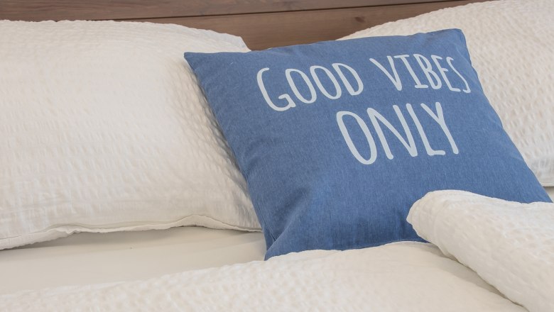 Doppelzimmer Fuchs, © A. Dirnbauer Bett mit blauem Kissen, Aufschrift 'Good Vibes Only'.