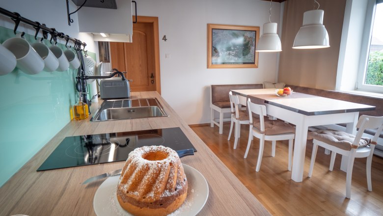 Wohnküche, © Doris Eminger Moderne Wohnküche mit Esstisch, Stühlen und Gugelhupf auf der Arbeitsplatte.