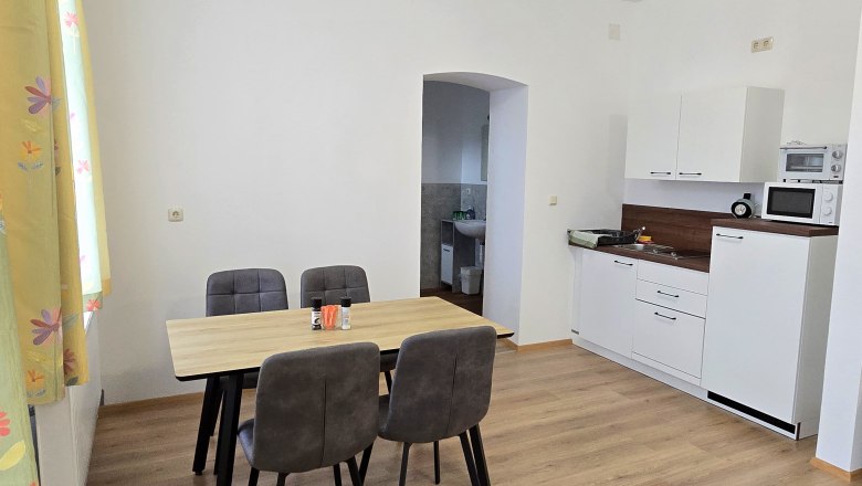 Apartment 3 - Essbereich und Küche, © Apartment Bauer Zur Alten Schule Essbereich mit Tisch und vier Stühlen, daneben eine kleine Küchenzeile mit Mikrowelle und Spüle.