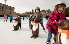 Kunsteisbahn Matzen, © Barbara P. Photography Kinder beim Schlittschuhlaufen mit Pinguin-Hilfen auf einer Eisbahn.