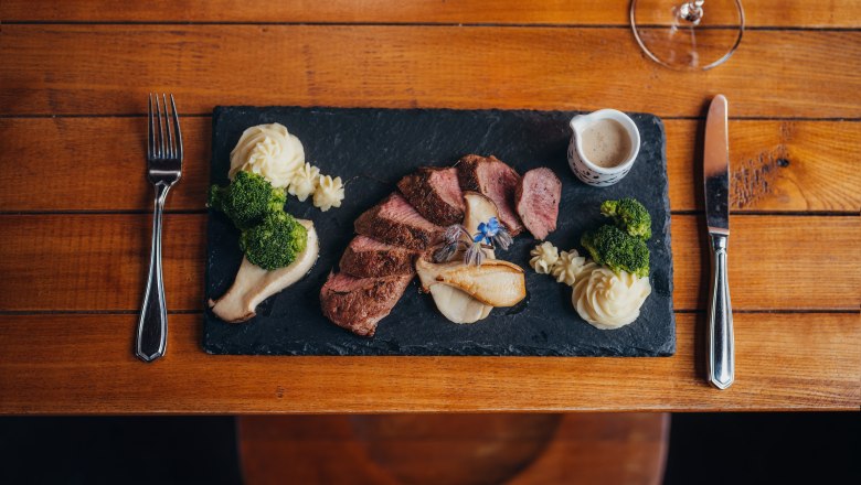 Rosa Hirschrücken, Grestner Austernsaitlinge, Trüffelpüree, Wacholderbeersoße, © Niederösterreich Werbung/Daniela Führer Gourmetgericht auf Schieferplatte mit Fleisch, Püree, Brokkoli und Soße.