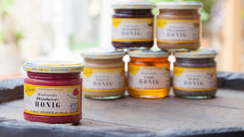 Honigsorten, © Imkerei Stögerer, Fotograf Gerhard Kapeller Verschiedene Honiggläser auf einem Tisch, im Vordergrund Himbeer-Honig.