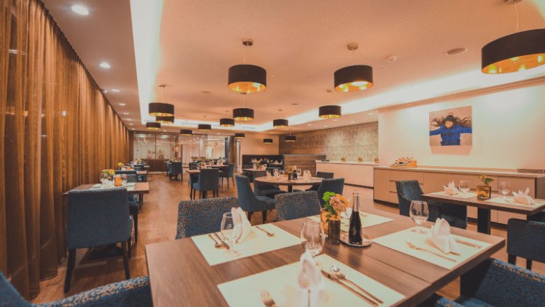 Restaurant, © NMC Elegantes Restaurant mit gedeckten Tischen, blauen Stühlen und moderner Beleuchtung.