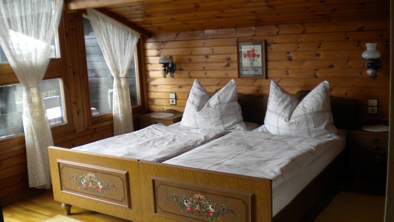 Schlafzimmer, © Weiß Gemütliches Schlafzimmer mit Holzwänden, Doppelbett und Spitzengardinen.