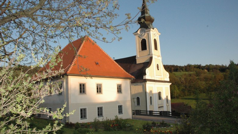 Kirche mit Pfarrhof, © Gemeinde St. Georgen/Leys Kirche mit Pfarrhof in ländlicher Umgebung, umgeben von Bäumen und Wiesen.