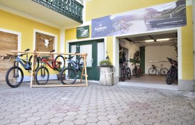 Bikeverleih Krumbacherhof, © Krumbacherhof Fahrradverleih mit mehreren Mountainbikes vor einem gelben Gebäude.