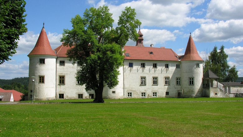 Gemeinde Dobersberg, © Gemeinde Dobersberg Ein historisches Schloss mit roten Dächern und Türmen, umgeben von grüner Wiese und Bäumen, unter einem blauen Himmel mit weißen Wolken.