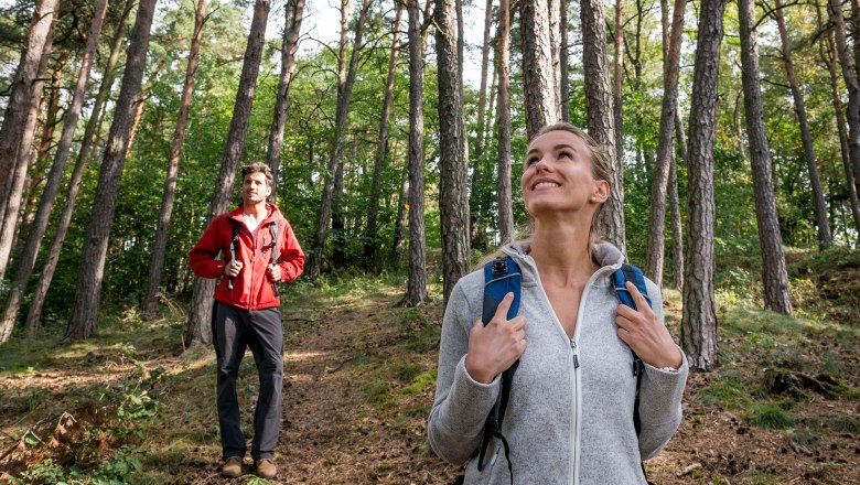 Wandern im Südlichen Waldviertel, © Waldviertel Tourismus, Studio Kerschbaum Zwei Personen wandern im Wald, eine Frau im Vordergrund lächelt, ein Mann im Hintergrund trägt eine rote Jacke.
