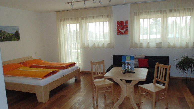 Zimmer, © Heiderer Helles Zimmer mit Doppelbett, Tisch, Stühlen und Sofa.