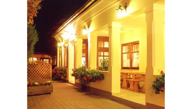 Heuriger Gilg, © Weingut Gilg Beleuchteter Eingangsbereich eines traditionellen Gebäudes mit Säulen und Blumen.