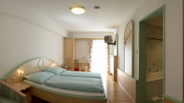 Standard Zimmer, © zVg Kirchenwirt Ein Hotelzimmer mit Doppelbett, Schreibtisch, Fernseher und Badezimmer.