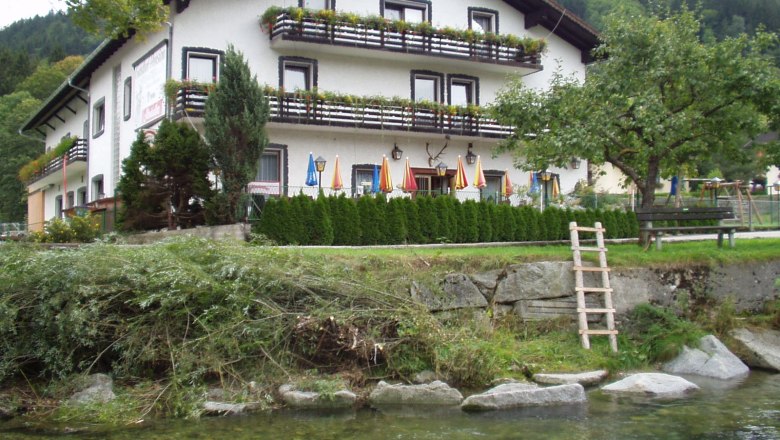 Gasthof Lichtensteg, © Archiv Betrieb Ein traditionelles Gasthaus mit Balkon und Blumenkästen, umgeben von Bäumen und einem Fluss im Vordergrund.