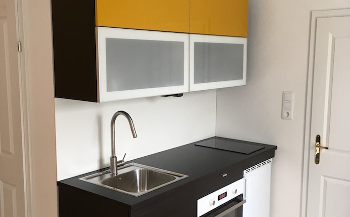 Alte Post Greifenstein, © Eduard Renfer Kleine moderne Küche mit gelben Oberschränken, Spüle, Herd und Backofen.