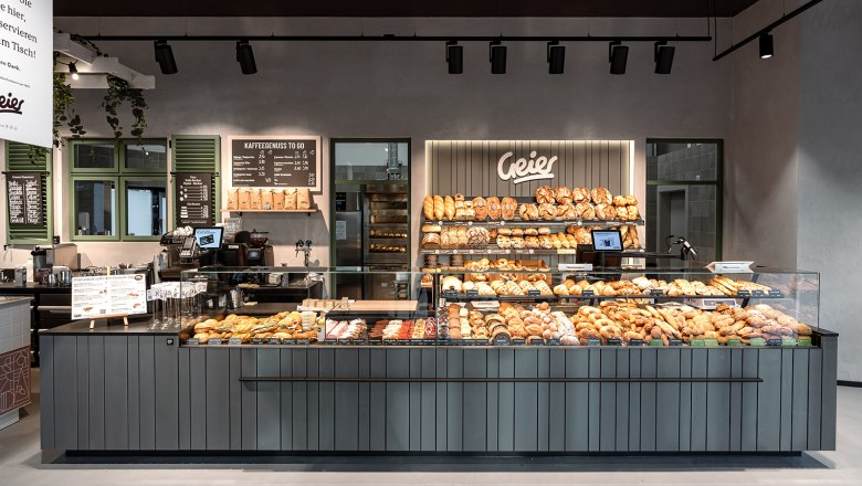 Kaffeehaus, © Geier.die Bäckerei Innenansicht einer modernen Bäckerei mit einer Theke voller Backwaren und einem Schild mit dem Namen Geier.