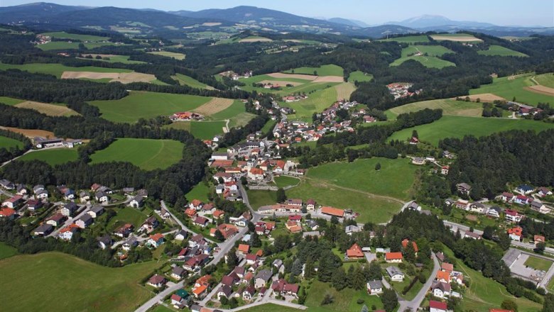 Ortsbild Zöbern, © Gemeinde Zöbern Luftaufnahme von Zöbern, einer ländlichen Gemeinde mit Häusern und Feldern, umgeben von Hügeln und Wäldern.