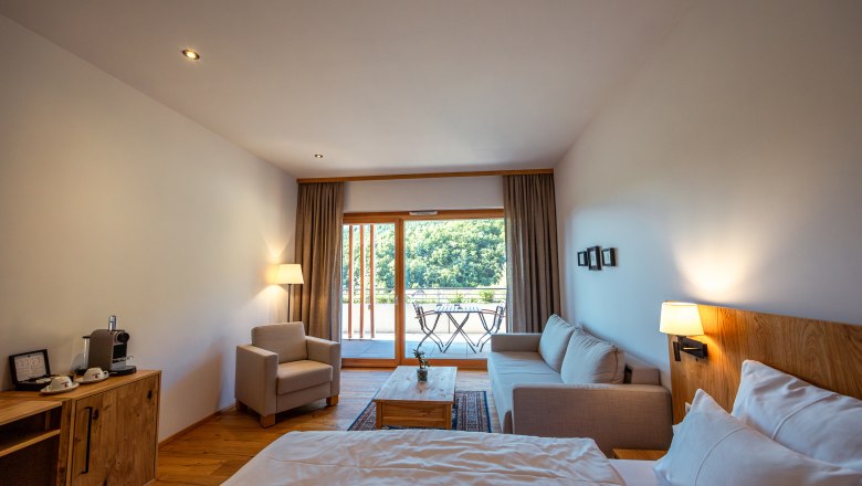 Weinhotel Nigl, © Niederösterreich Werbung / Maximilian Pawlikowsky Modernes Hotelzimmer mit Bett, Sofa, Sessel und Balkon mit Blick ins Grüne.