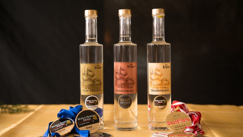 Edelbrände, © Wirtshausbrennerei Krenn Drei Flaschen Edelbrand mit Medaillen auf einem Tisch.
