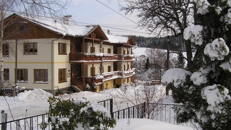 Ofnerhof St. Corona am Wechsel, © familie-gruber Ein verschneites Gebäude mit Holzbalkonen in einer winterlichen Landschaft.