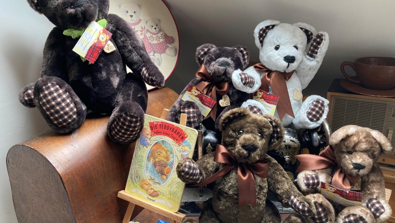 Bärenfamilie, © Elisabeth Seitner Eine Sammlung von Teddybären auf einem Tisch, umgeben von Dekorationen und einem Buch über Teddybären.