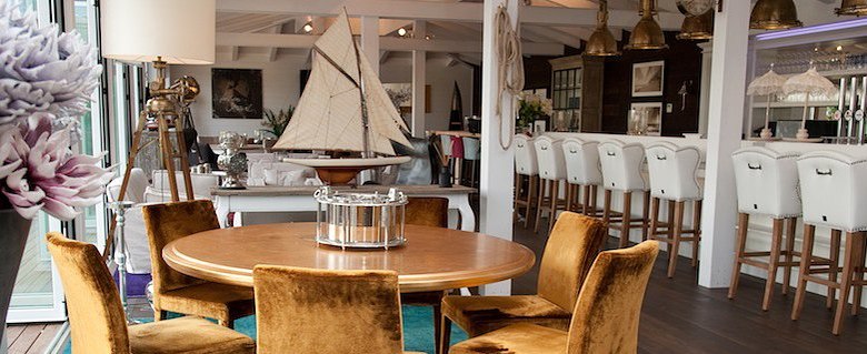 Barbereich, © Diamond Club Atzenbrugg Eleganter Barbereich mit runden Holztischen, samtigen Stühlen und einer Bar mit weißen Hockern.