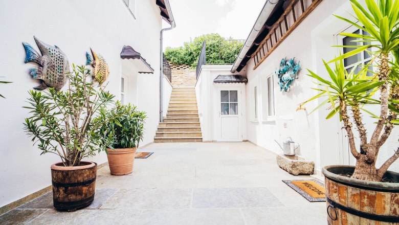 Roth0_1, © Georg Pomassl Heller Innenhof mit Treppe, Pflanzen in Töpfen und Fischdekorationen an den Wänden.