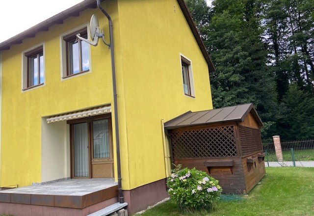 Ferienhaus am Schloßpark, © Wiener Alpen Gelbes Ferienhaus mit Terrasse und kleinem Anbau, umgeben von Bäumen.