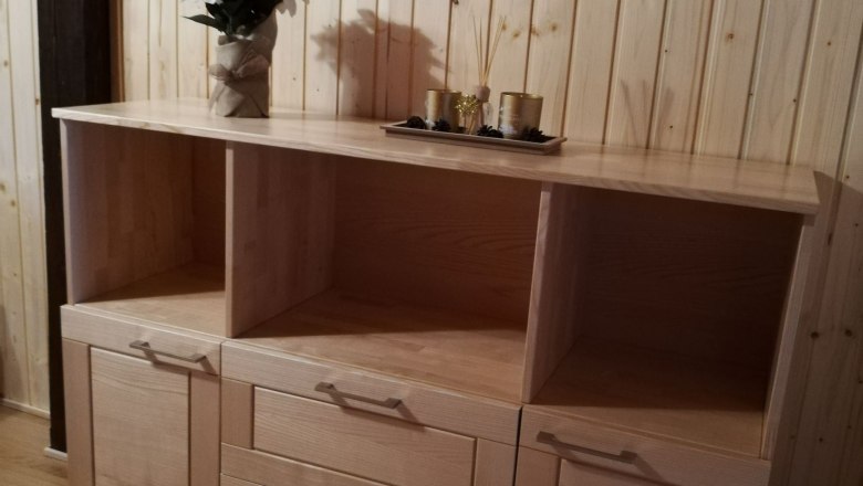 Dachgeschoss Apartment, © Familie Weibels Holzkommode mit Dekoration in einem Raum mit Holzvertäfelung.