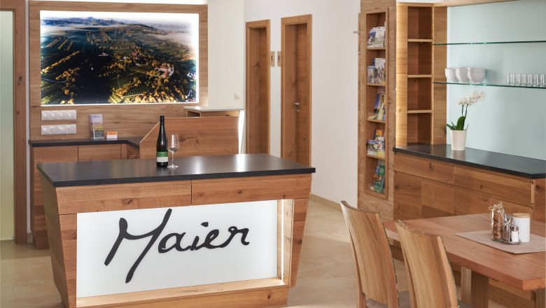 Weinhof Maier, © Weinhof Maier Innenansicht eines modernen Empfangsbereichs mit Holzmöbeln und einem großen Landschaftsbild an der Wand.