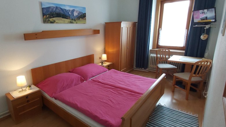 Doppelzimmer, © Martin Zwinz Ein gemütliches Doppelzimmer mit Holzmöbeln, einem Doppelbett mit pinker Bettwäsche, einem Tisch mit zwei Stühlen und einem kleinen Fernseher.