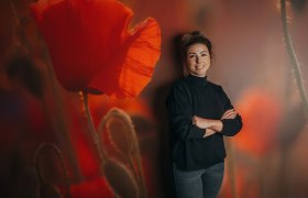 Wirtin Stefanie Eilnberger-Schreiner, © Niederösterreich Werbung/Daniela Führer Frau steht vor einer Wand mit Mohnblumenmotiv.