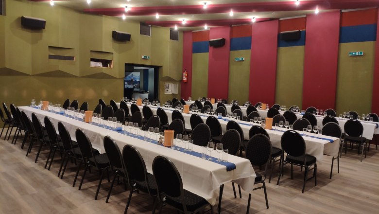 Tafel im Saal, © Markus Kiener Ein großer Saal mit langen, gedeckten Tischen und schwarzen Stühlen, bereit für ein Event.