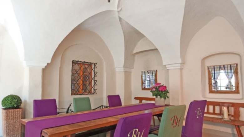 Renaissancehotel Raffelsberger Hof, © Renaissancehotel “ Raffelsberger Hof “ Innenansicht eines Raumes im Renaissancehotel Raffelsberger Hof mit gewölbter Decke, Holztisch und Stühlen mit lila und grünen Bezügen.