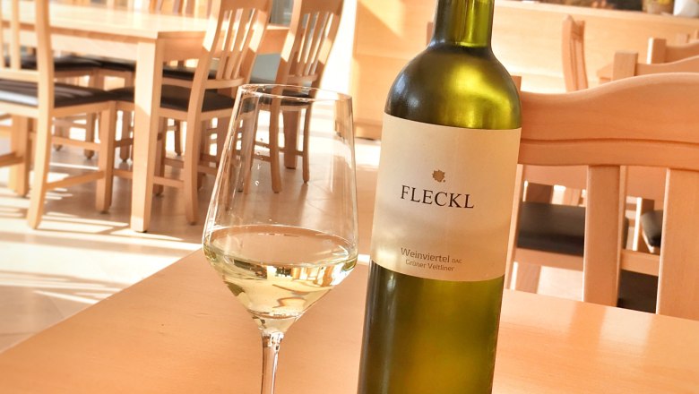 Verkostungsraum, © Alexander Fleckl Eine Flasche Weißwein und ein gefülltes Weinglas auf einem Holztisch in einem Verkostungsraum.