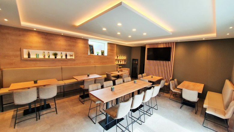 Moderner Verkostungsraum, © Weingut Schwinner Moderner Verkostungsraum mit Holztischen, gepolsterten Stühlen und dekorativen Regalen mit Flaschen.