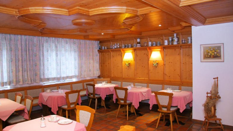 Frühstücksraum, © Haus am Mühlfeld Gemütlicher Frühstücksraum mit Holzmöbeln, rosa Tischdecken und dekorativen Krügen auf einem Regal.