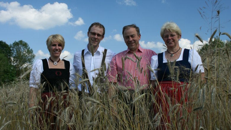 Familie Zimmermann, © Zimmermann Vier Personen in traditioneller Kleidung stehen in einem Getreidefeld unter blauem Himmel.