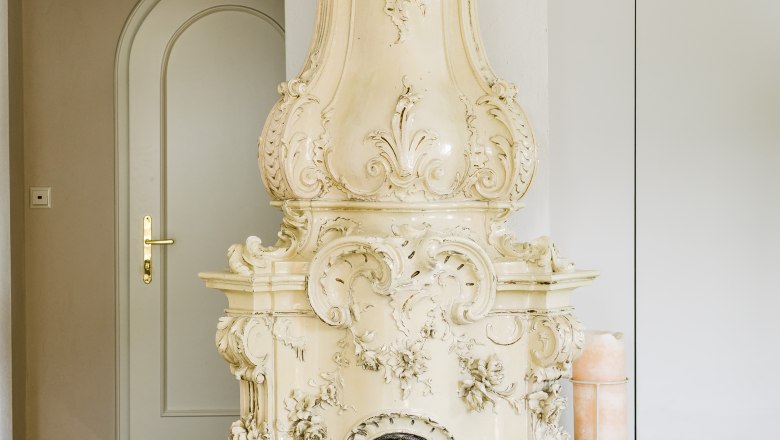 villa_schonthal-15_3, © Julius Hirtzberger Ein kunstvoll verzierter, antiker Kaminofen in einem Raum mit Fliesenboden.