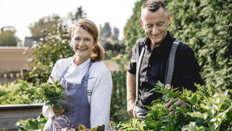 Wirtin Alexandra Labenbacher-Konecny im großen Wirtshausgarten, © Niederösterreich Werbung/David Schreiber Zwei Personen stehen in einem Garten, eine Frau in Kochkleidung hält Kräuter.