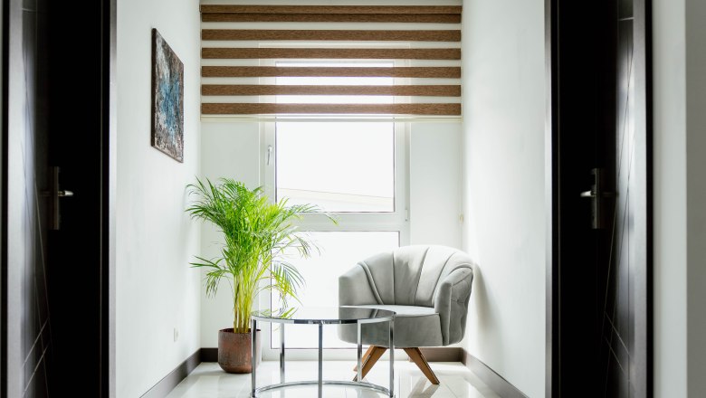 Hotel Lamede, © Hotel Lamede Helle Ecke mit Sessel, Glastisch und Pflanze vor einem Fenster mit Jalousien.