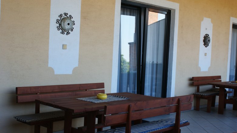 Privatzimmer Würger, © Privatzimmer Würger Terrasse mit Holztischen und Bänken, dekoriert mit Wandornamenten.