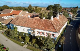 Schloss Zogelsdorf, © Waldviertel Tourismus, lichtstark.com Luftaufnahme eines historischen Gebäudes mit roten Ziegeldächern und weißen Fassaden, umgeben von Bäumen und Straßen.