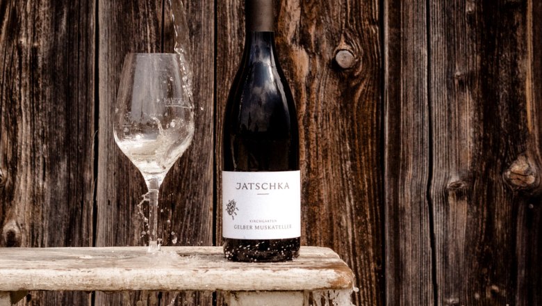 Weingut Jatschka, © Astrid Bartl Weinflasche und Glas mit Wasser vor Holzwand.