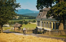 Grenzlandroute beim Schloss Ziegersberg in Zöbern, © Wiener Alpen, Philipp Schönauer Eine Radfahrerin auf einer Landstraße fährt am Schloss Ziegersberg vorbei. Im Hintergrund der Wechsel.