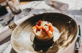 Das Linsberg - Restaurant, © Linsberg Asia Ein kunstvoll angerichtetes Gericht auf einem braunen Teller in einem Restaurant.