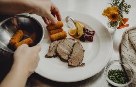 Wirtshausküche mit Spezialitätenwochen, © Niederösterreich Werbung/Rita Newman Ein Teller mit Fleisch, Kroketten, Preiselbeeren und Zitronenscheiben wird angerichtet.