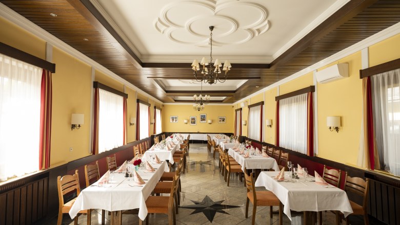 Einkehre – für Feste aller Art, © Niederösterreich Werbung/Michael Reidinger Ein festlich gedeckter Speisesaal mit gelben Wänden, Holzmöbeln und weißen Tischdecken.